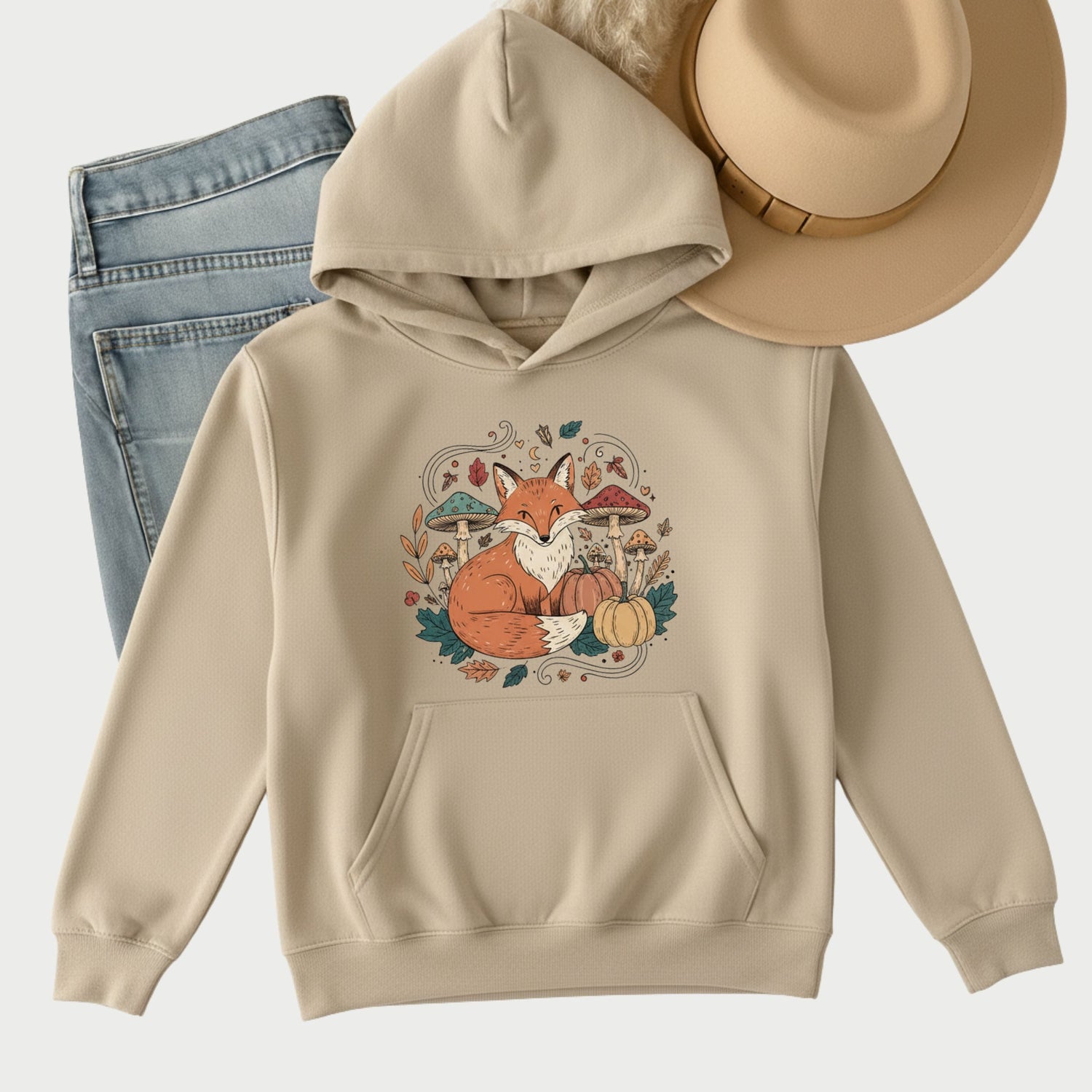 Flat lay of a sand-colored hoodie sweatshirt with blue jeans and a tan hat, styled for a cozy winter outfit.