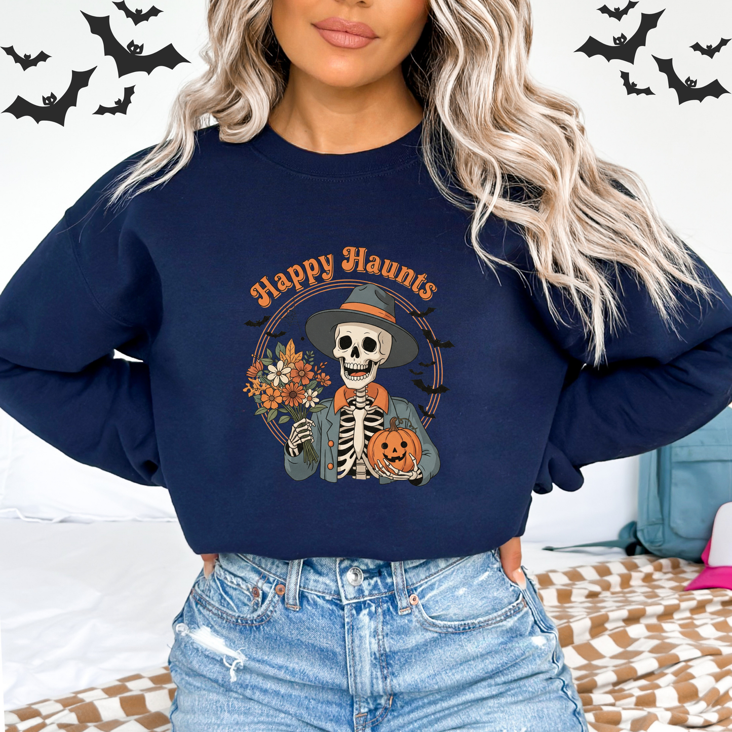 Person wearing a navy blue sweatshirt with 'Happy Haunts' and skeleton design, surrounded by Halloween decorations.