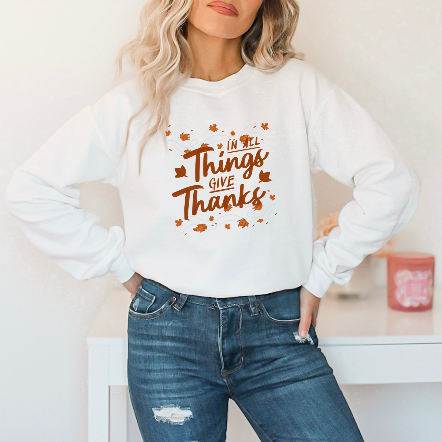 Person wearing a white sweatshirt with 'In All Things Give Thanks' text and autumn leaves.