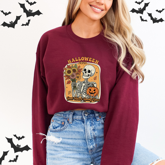 Person wearing a maroon sweatshirt with Halloween-themed design, Person wearing a yellow Halloween sweatshirt with a skeleton holding flowers and pumpkin with Letter Halloween 2025 Good Vibes & Spooky Times design
