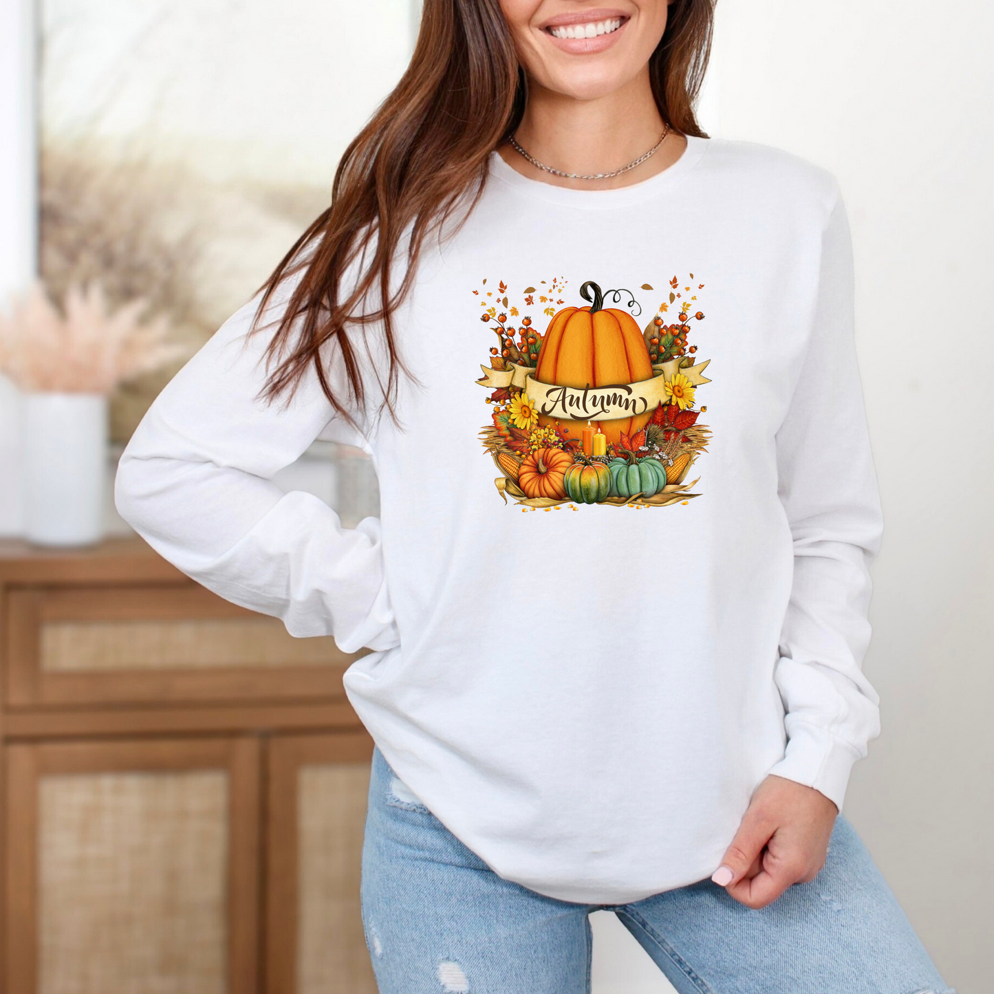 Person wearing a white sweatshirt with an autumn-themed design featuring pumpkins and leaves.