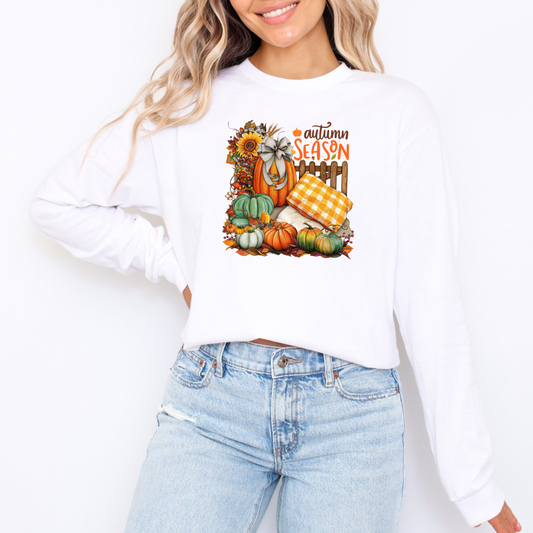 Person wearing a white sweatshirt with an autumn-themed graphic design on a plain background featuring with letter Autumn Season
