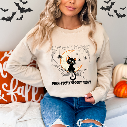 Person wearing a cream sweatshirt with a Halloween design featuring a black cat, moon, and text.