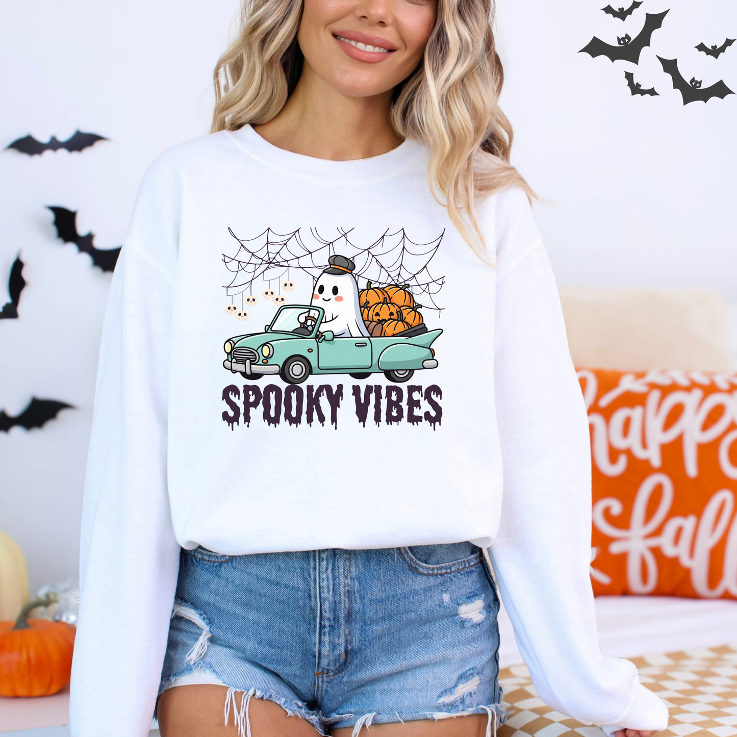 Person wearing a white sweatshirt with a Halloween-themed design, including a ghost in a car and pumpkins, with text 'Spooky Vibes'.