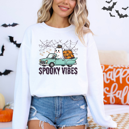 Person wearing a white sweatshirt with a Halloween-themed design, including a ghost in a car and pumpkins, with text 'Spooky Vibes'.