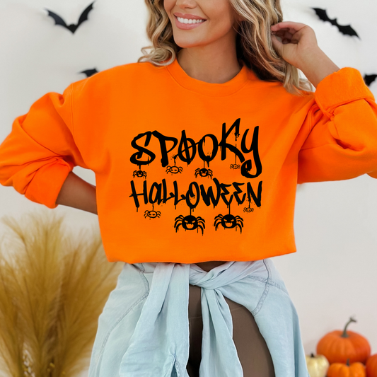 Person wearing an orange sweatshirt , A bold, graffiti-style text illustration that reads "SPOOKY HALLOWEEN" in a dripping font, with various spiders hanging around and crawling on the letters. The design is predominantly black with a distressed or splattered effect.