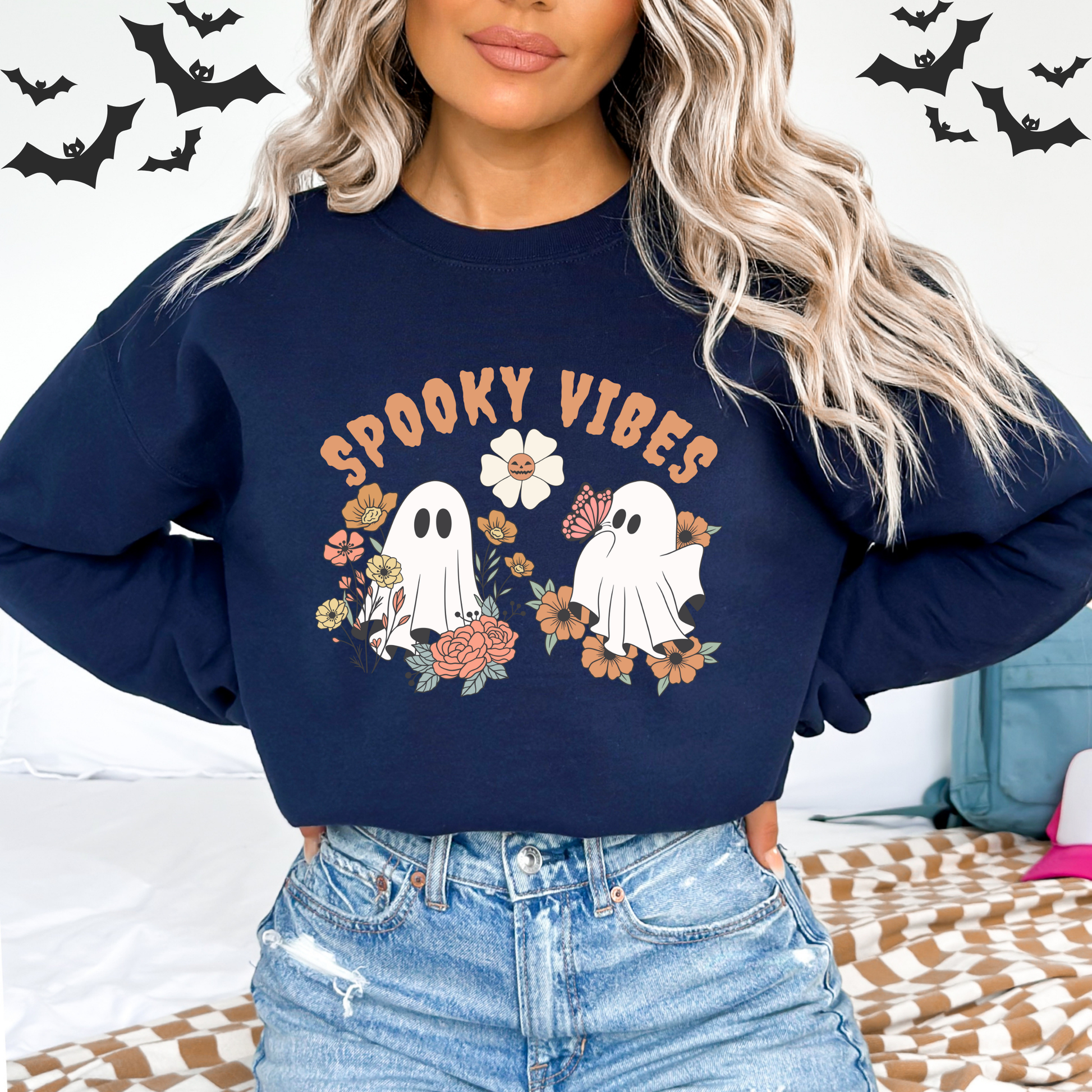 Person wearing a navy blue sweatshirt with 'Spooky Vibes' and ghost graphics, surrounded by Halloween decorations.